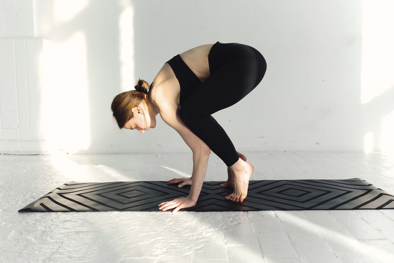 Yoga practitioner balancing in crow pose in a sunlit studio room