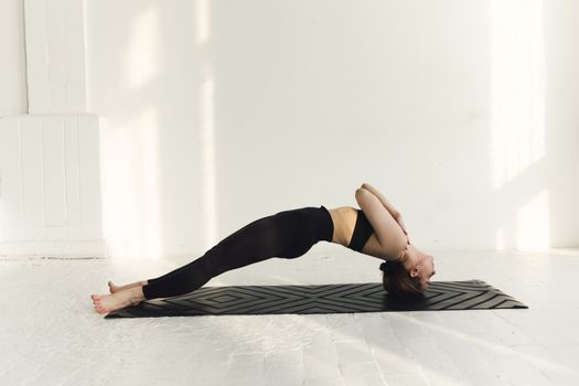 A woman performing a yoga pose on a mat in a minimalist indoor setting.