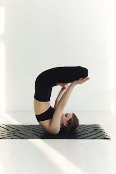 Woman in black activewear practicing a yoga pose on a mat indoors. Perfect for fitness and mindfulness themes.