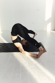 A woman demonstrating a challenging yoga pose on a mat in a sunlit room, symbolizing balance and flexibility.