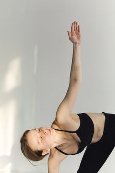 Young woman in black sportswear practicing Trikonasana yoga pose indoors.
