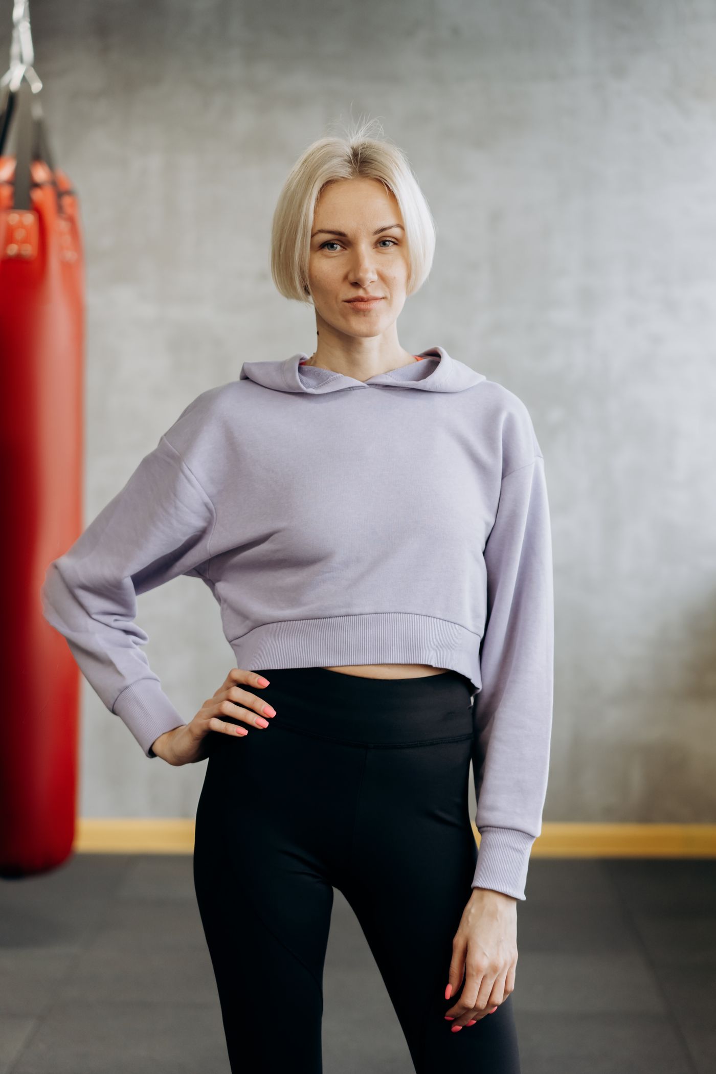 Woman in a lilac cropped hoodie standing beside a punching bag