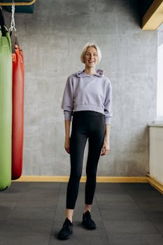 Happy female athlete in sporty attire standing confidently in a stylish gym environment.