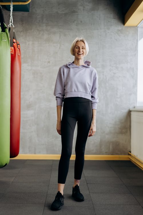Free Happy female athlete in sporty attire standing confidently in a stylish gym environment. Stock Photo