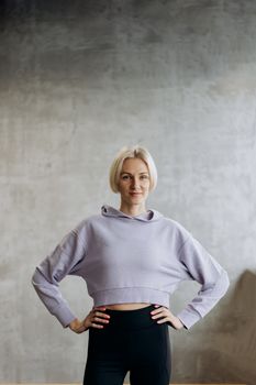 Confident woman in lavender hoodie posing with hands on hips indoors.