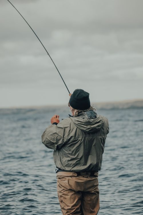 Free Man wearing a jacket and knit cap fishing in the ocean, showcasing outdoor adventure. Stock Photo