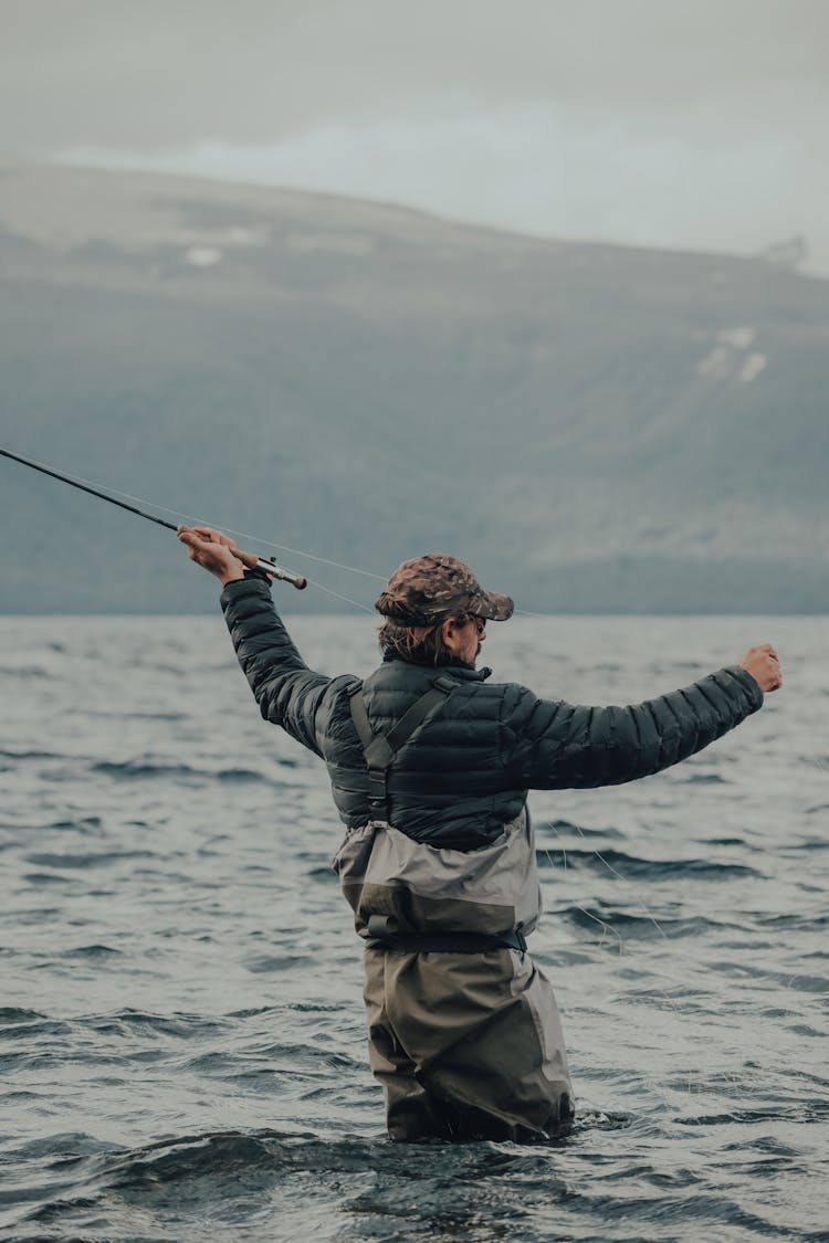 Man In Black Jacket And Brown Pants Holding Black Fishing Rod