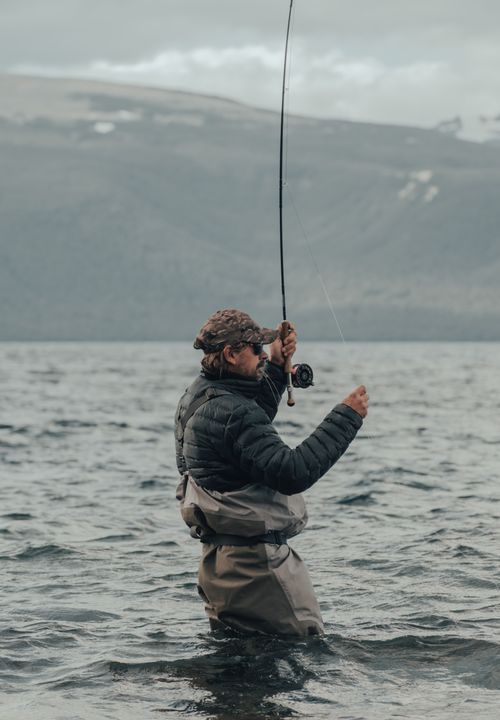 Free An adult fly fisherman standing knee-deep in a mountain lake, casting a fishing line. Stock Photo