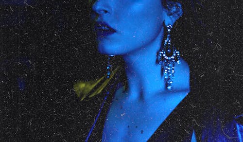 Extravagant woman in massive sparkling earrings in blue neon light