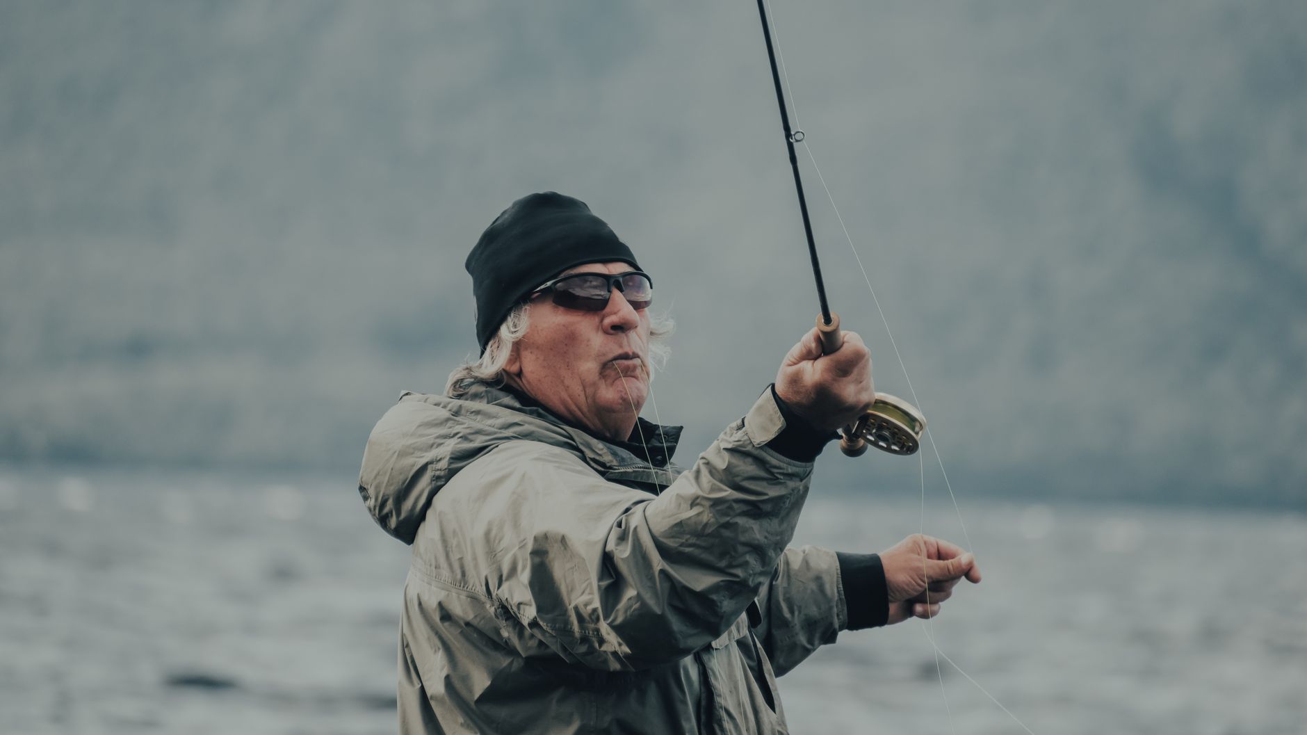 A senior man engaging in fly fishing by a lake, showcasing leisure and recreation outdoors.