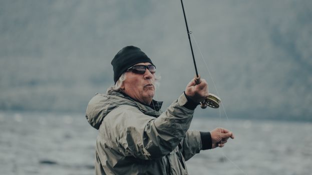 A senior man engaging in fly fishing by a lake, showcasing leisure and recreation outdoors.