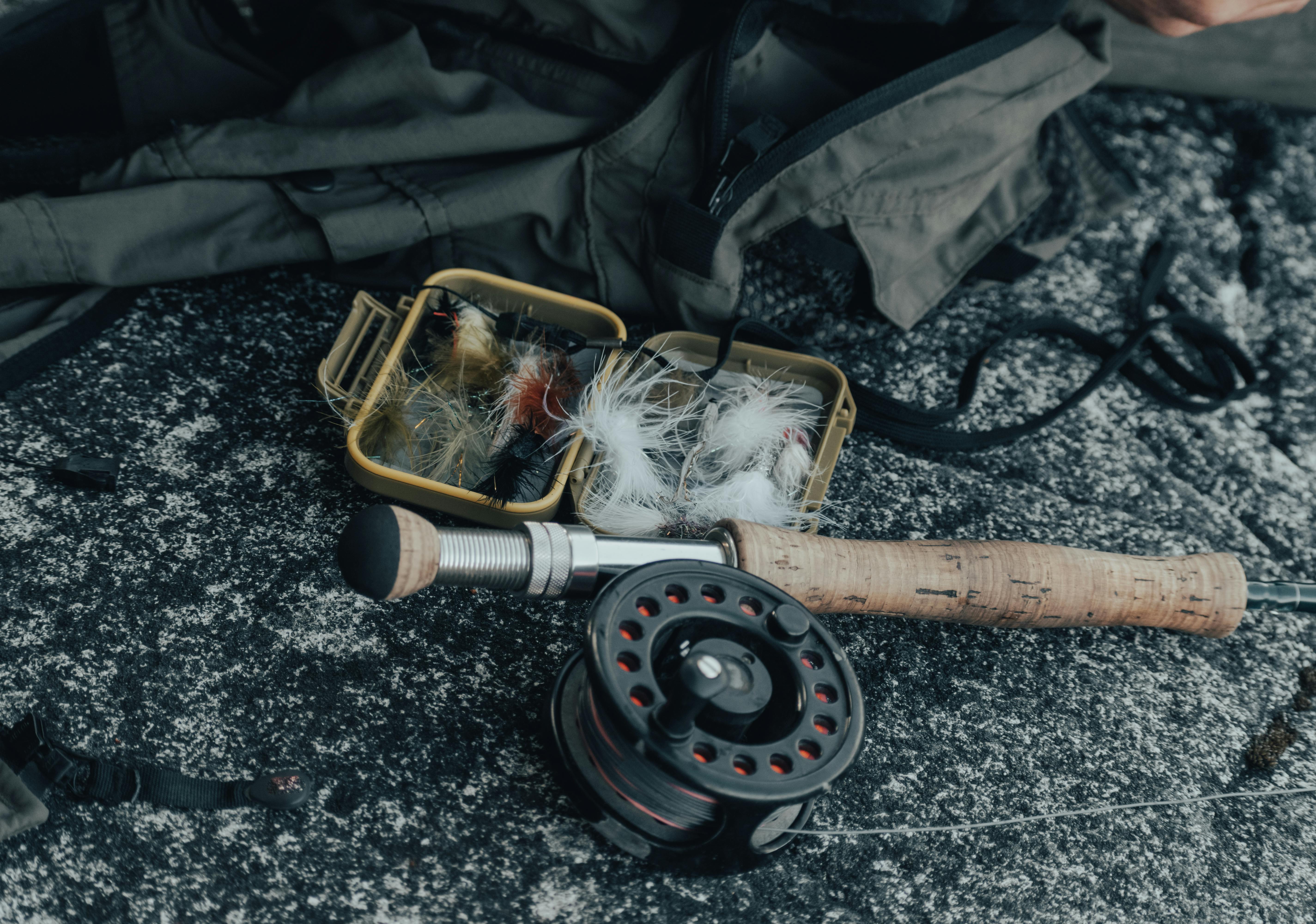 Close-up of fly fishing equipment including rod, reel, and a box of fly lures captured outdoors.