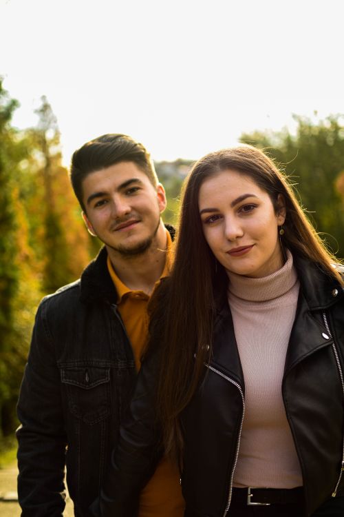 Free Young couple enjoying a sunny day outdoors with green trees in the background. Stock Photo