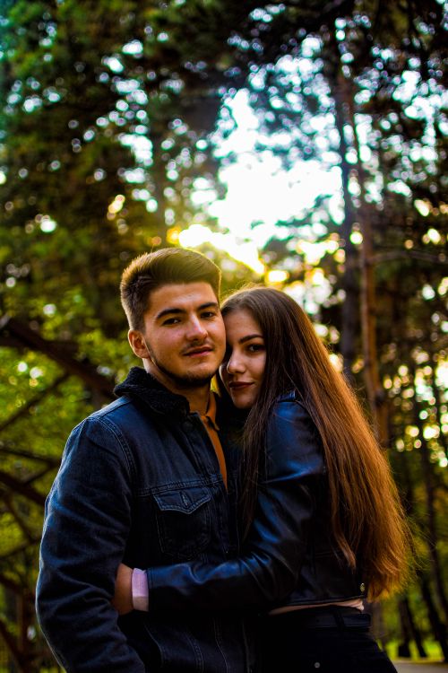 Free A couple warmly embraces outdoors with sunlight filtering through trees, showcasing romance and connection. Stock Photo