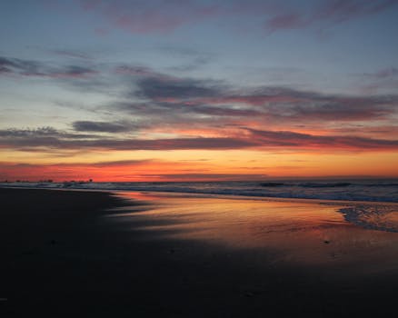 A glowing sunrise over a tranquil beach with a dramatic sky and reflective waves.