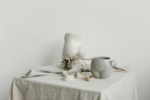 Elegant minimalist still life featuring a porcelain mug, ceramic sculpture, and soft linen drape.