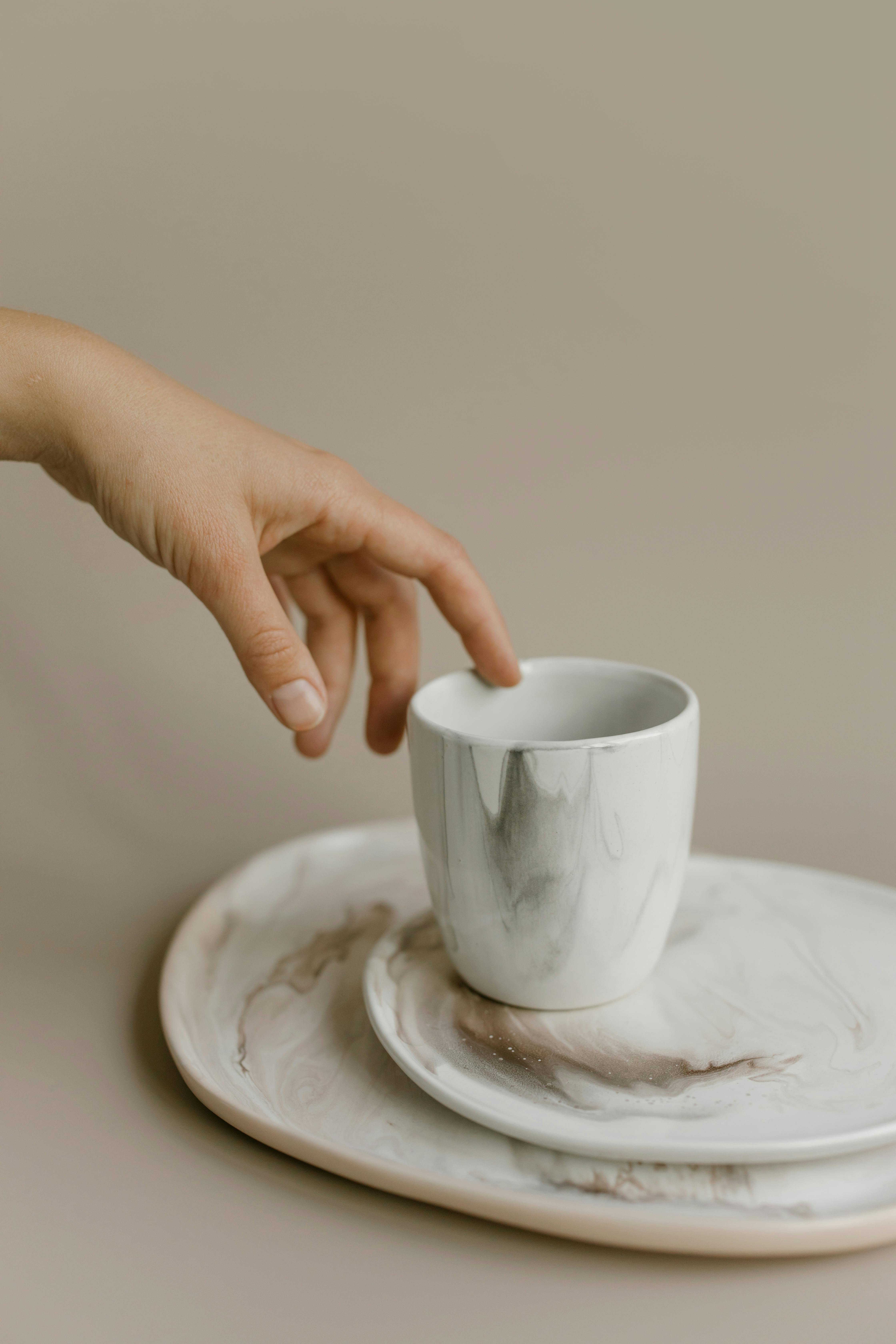 Minimalist ceramic set with a hand reaching for an elegantly designed cup.