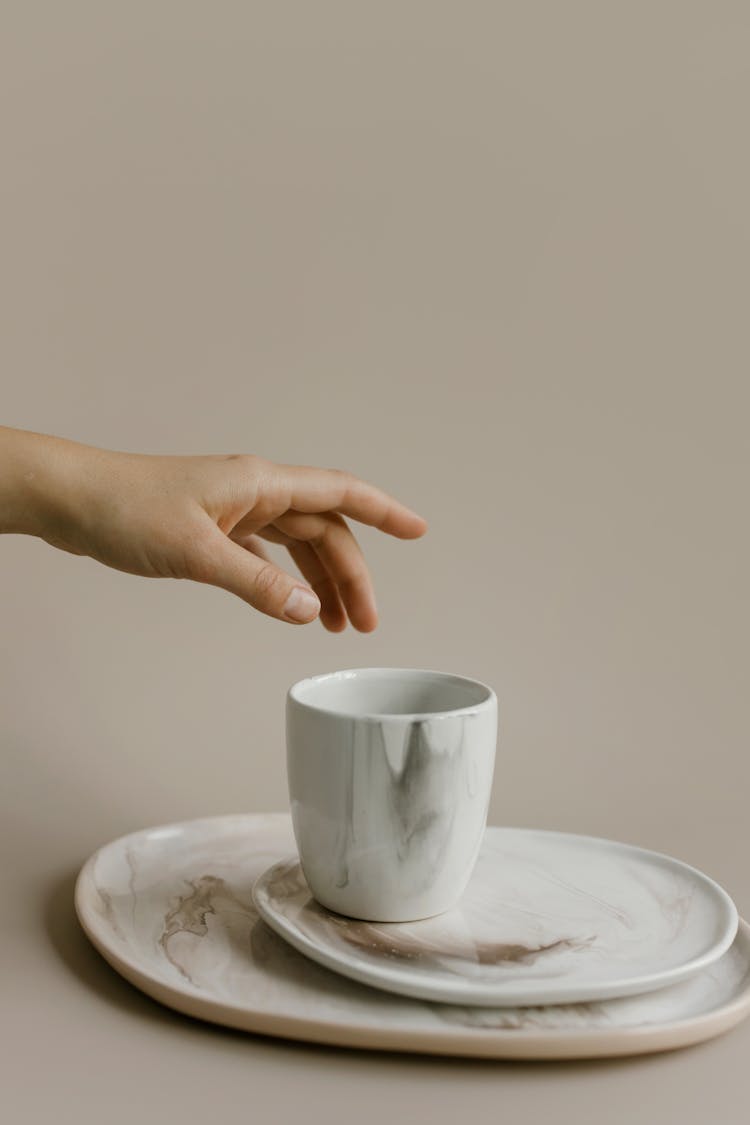 Photo Of A Person's Hand Reaching For A Ceramic Cup