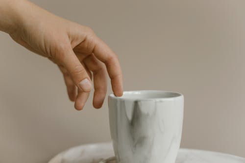 Free Close-Up Photo of a Person's Hand Touching a Ceramic Cup Stock Photo