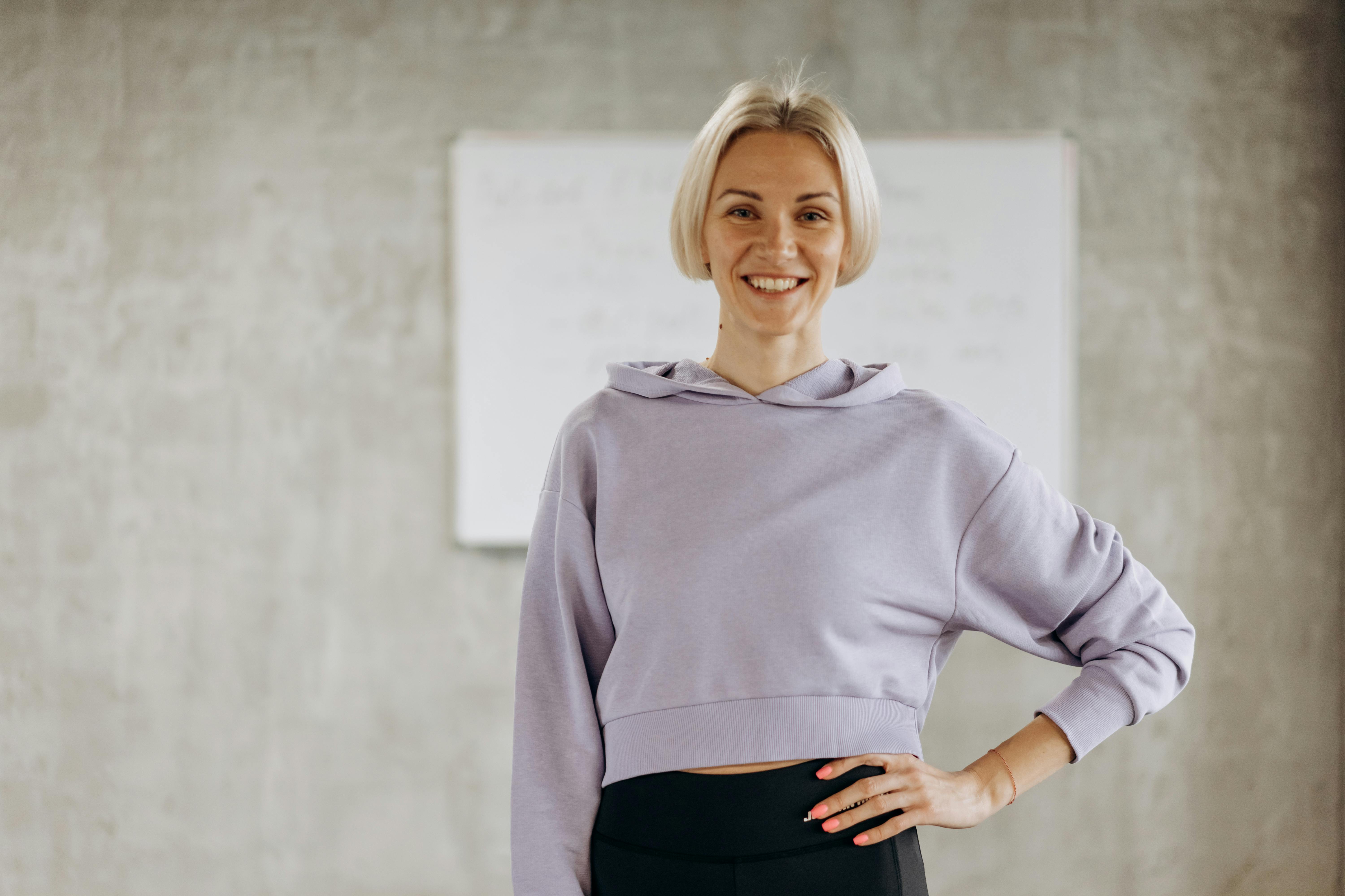 Happy woman in fitness wear poses confidently indoors, promoting healthy lifestyle and exercise.