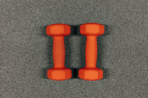 Free A close-up image of orange dumbbells on a textured gray surface, ideal for fitness themes. Stock Photo