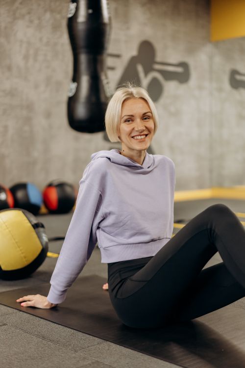 Free Fit and healthy woman smiling while stretching on a gym mat with exercise equipment around. Stock Photo