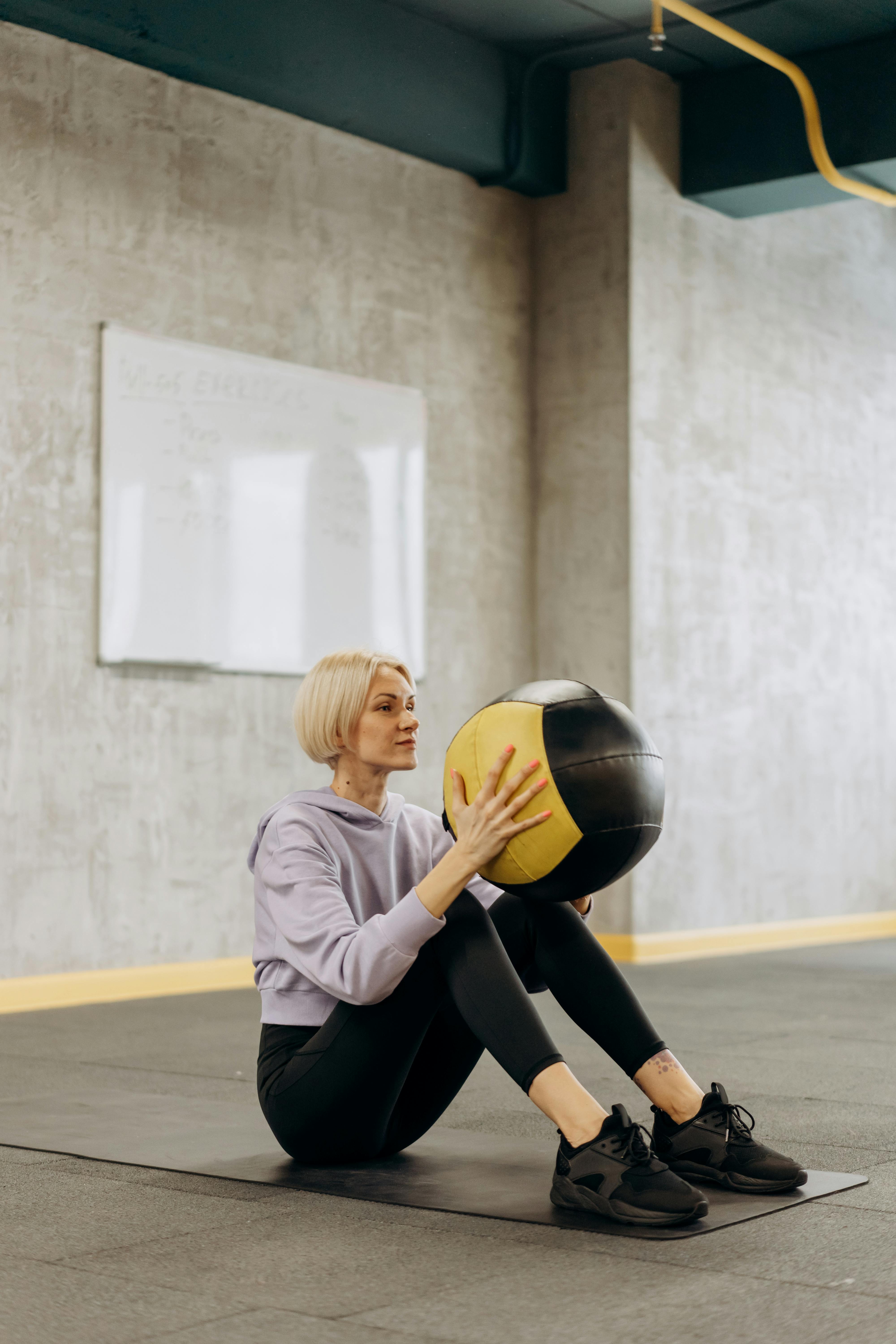 woman sitting on a mat with a ball on her knees