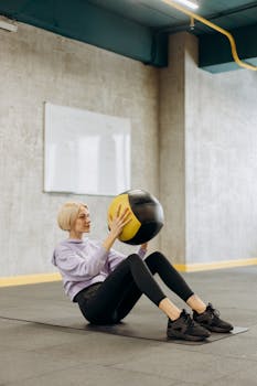 Fit woman balancing with a medicine ball during workout in modern gym setting.