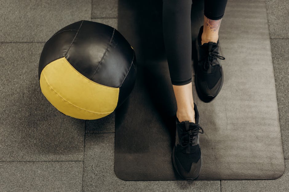 A woman sits on a gym mat with a medicine ball, ready for fitness training.