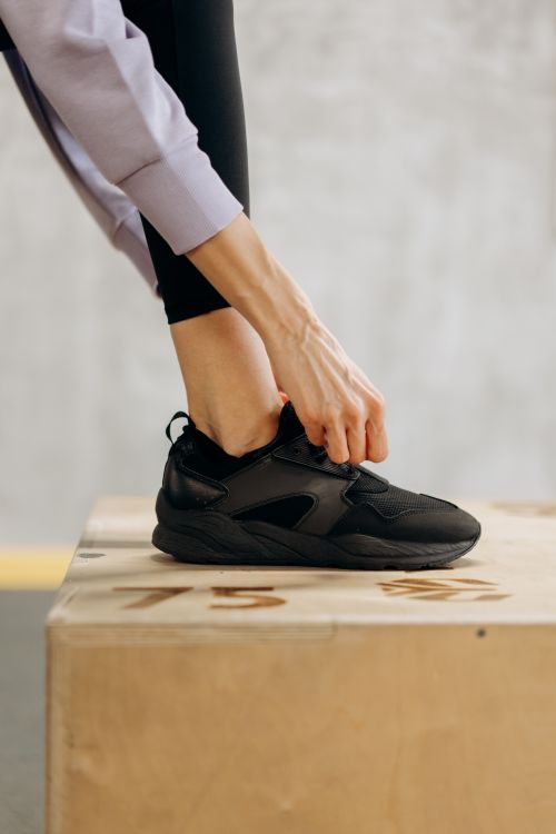 Free Close-up of a woman tying her black sneakers on a workout platform indoors. Stock Photo