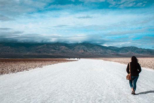 Woman walking alone on a salt flat with mountains in the background under a blue sky.