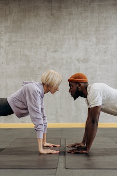 Two adults face off in a plank exercise on gym mats, embodying fitness and diversity.