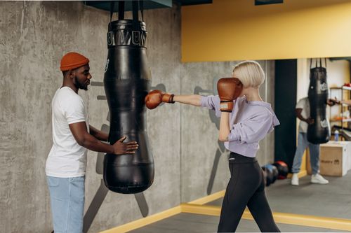 Free A female boxer training with a coach indoors, hitting a punching bag energetically. Stock Photo