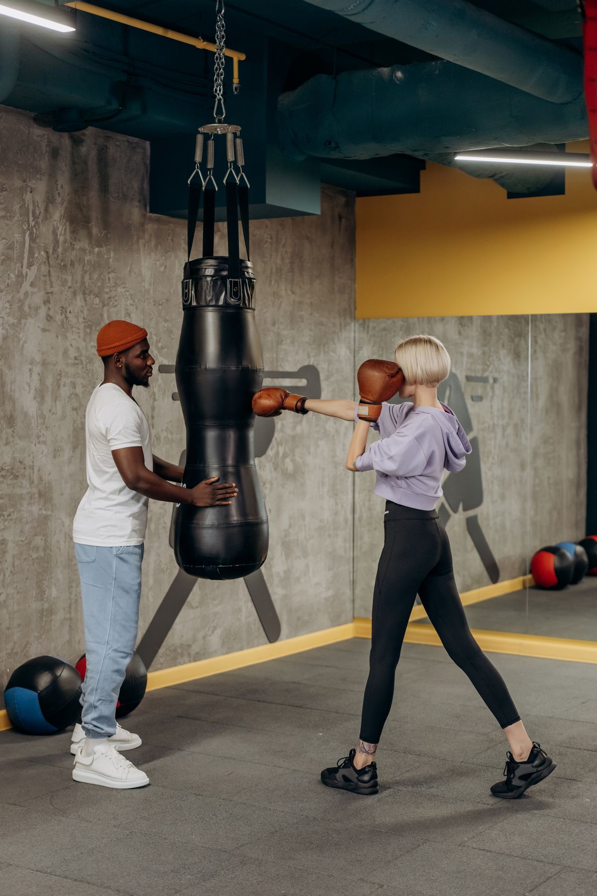 Boxtraining im Gym: Ein Trainer hält den Sandsack, eine Sportlerin schlägt mit Boxhandschuhen dagegen