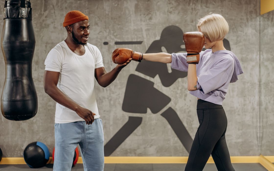 Woman in boxing gloves practising punches with her coach in a gym