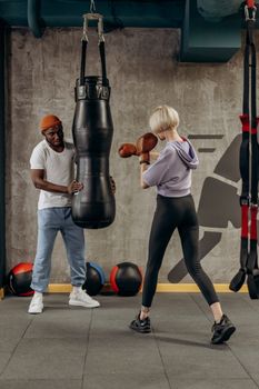 A woman practices boxing with a trainer holding a punching bag in an indoor gym.