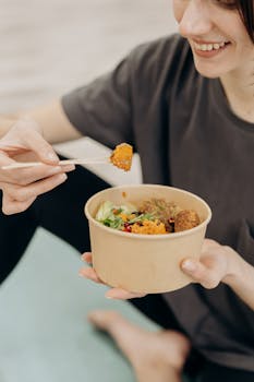 Smiling woman enjoying a nutritious meal in a bowl with chopsticks, promoting a healthy lifestyle.