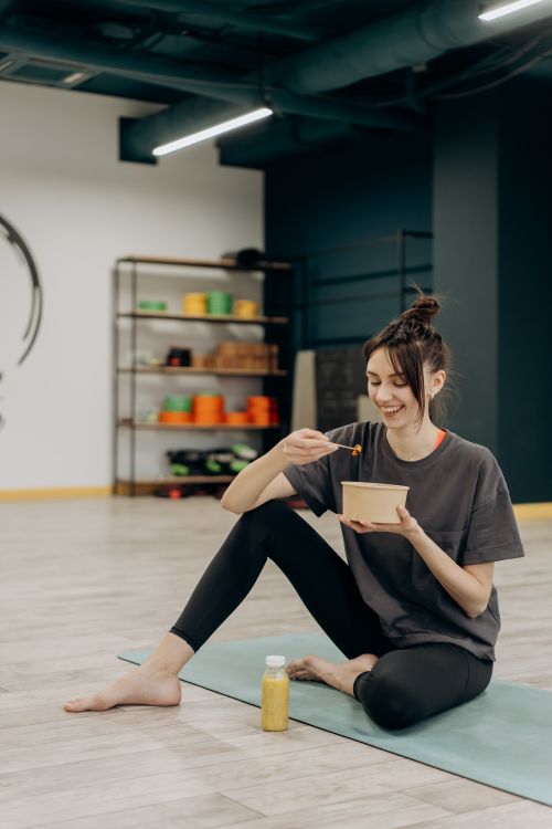 Free A smiling woman sitting on a mat enjoying a healthy meal indoors after exercise. Stock Photo