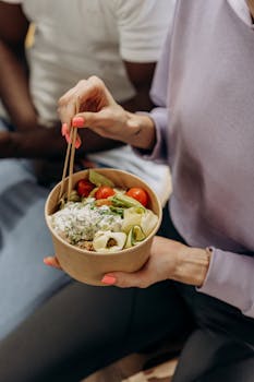 Person enjoying a nutritious salad bowl with fresh ingredients using chopsticks indoors.