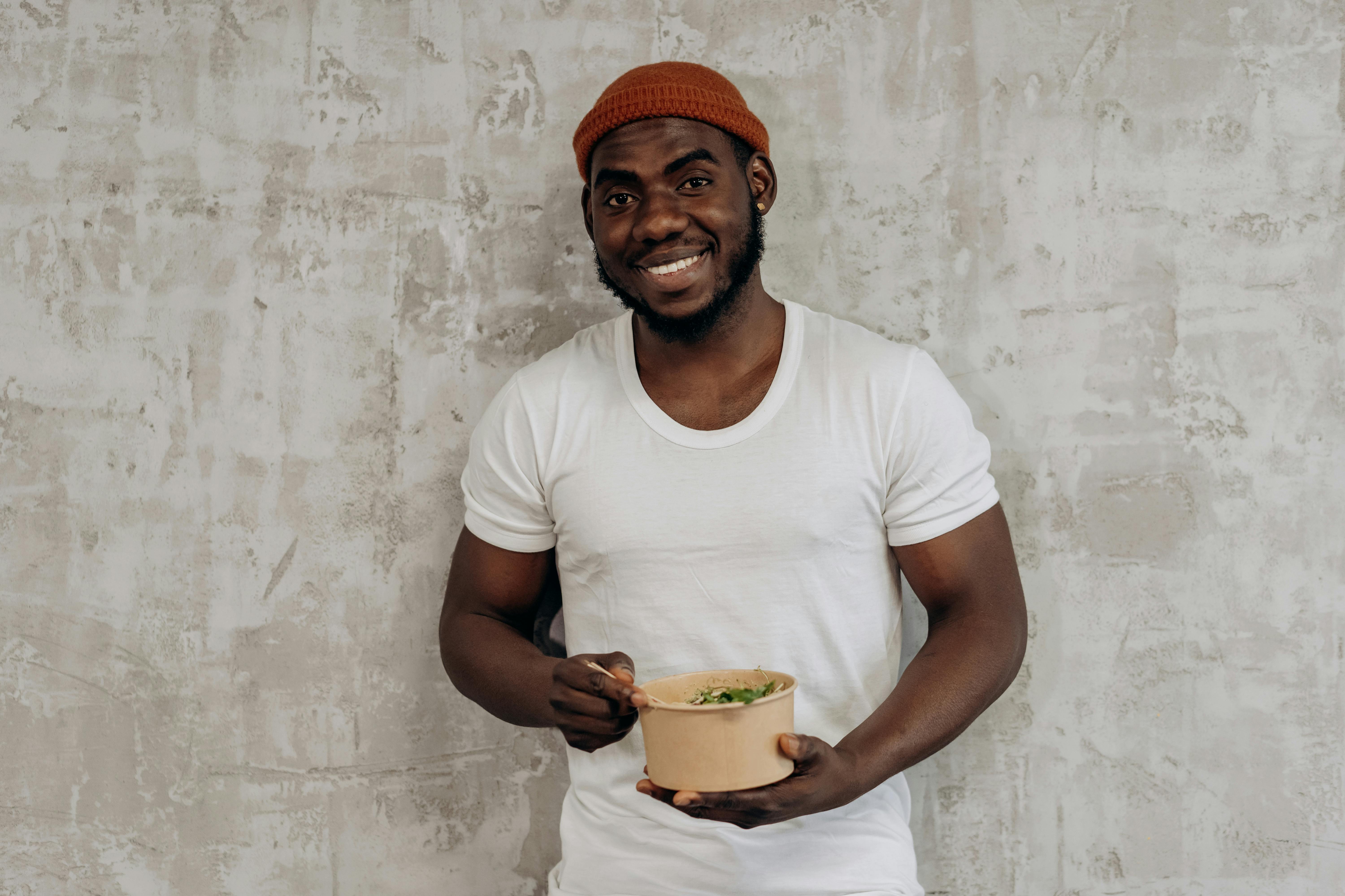 A happy man in a white shirt holding and enjoying a fresh salad indoors.