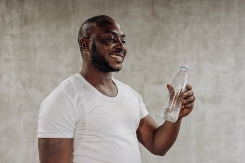 Man in White Crew Neck T-shirt Holding Clear Glass Bottle