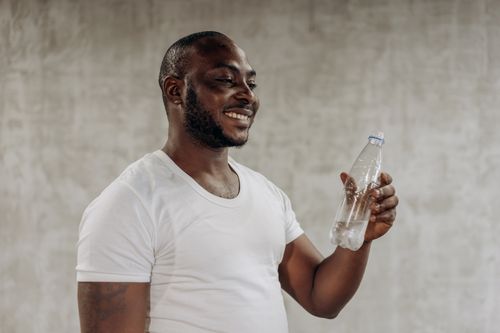 Free A happy man smiles while holding a bottle of water indoors, embracing healthy living. Stock Photo