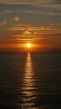 A breathtaking view of the sun setting over the ocean, casting vibrant orange hues across the sky and water.