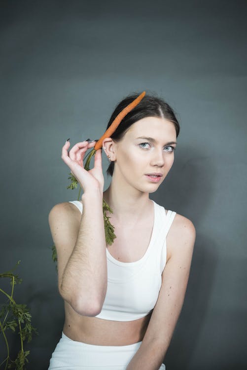 Free Woman in White Tank Top Holding a Carrot Stock Photo