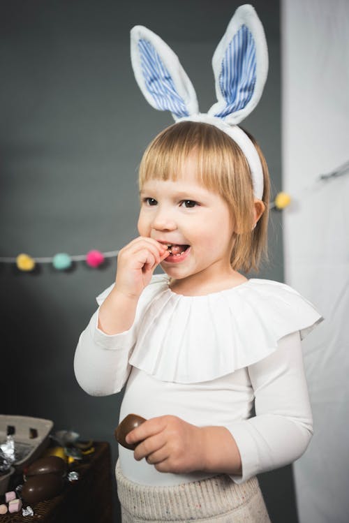 A Girl Wearing a Bunny Ears Headband Smiling While Eating Chocolates