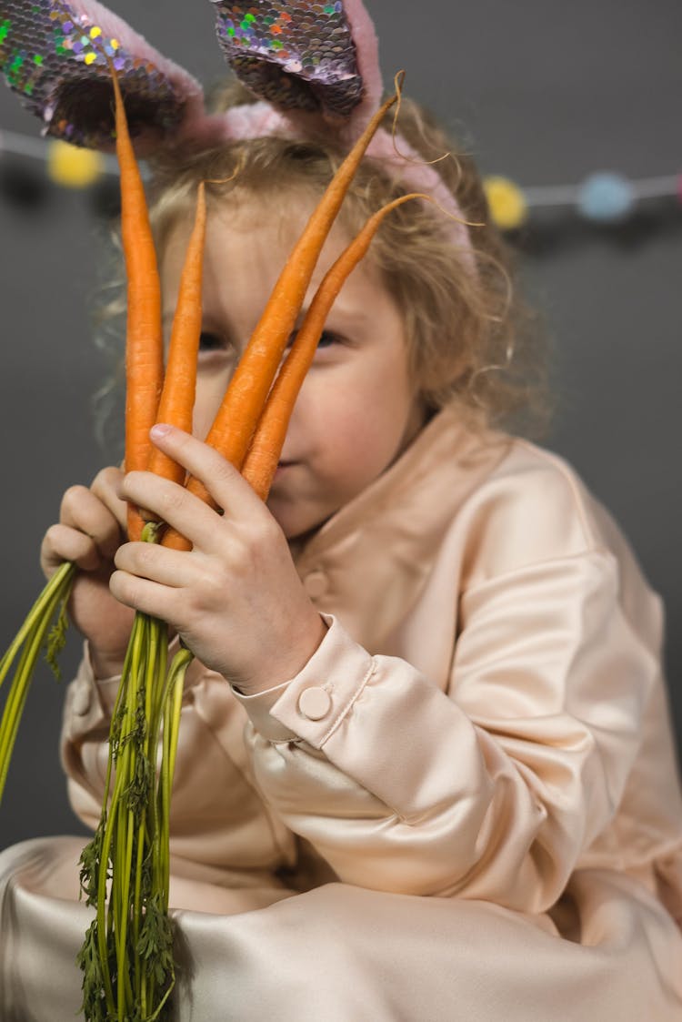 A Child Holding Carrots To Her Face