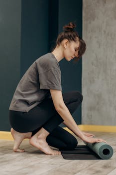 Woman setting up her yoga mat indoors, ready for a meditative exercise session.