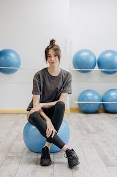 A young woman sitting on a yoga ball in a gym, exemplifying fitness and balance.