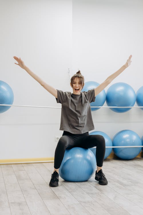 Free Woman Sitting On A Yoga Ball With Arms Raised Stock Photo