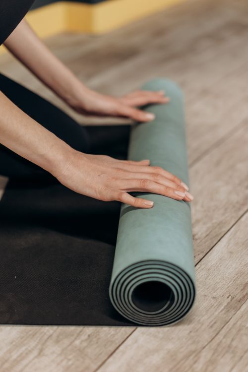 Free Close-up of woman's hands rolling up a yoga mat after practice. Stock Photo